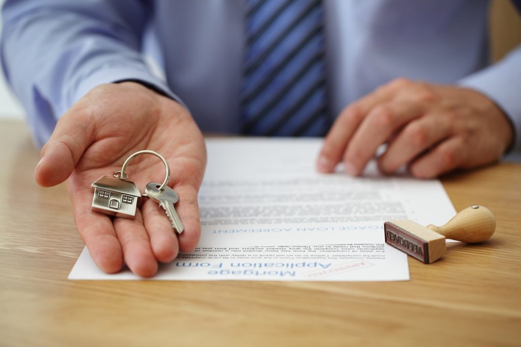 Key with house keychain being handed with mortgage form