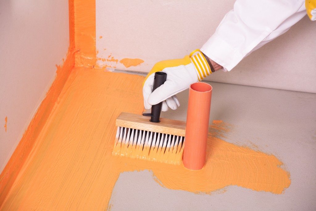 builder with brush applies waterproofing on the floor of the bathroom