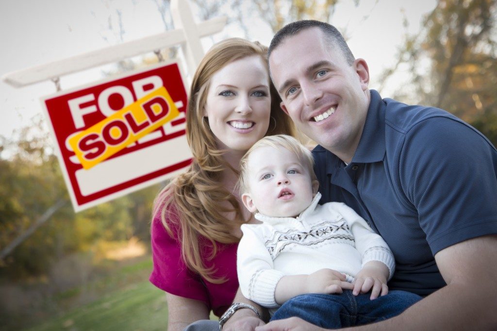 Happy Young Caucasian Family in Front of Sold Real Estate Sign.