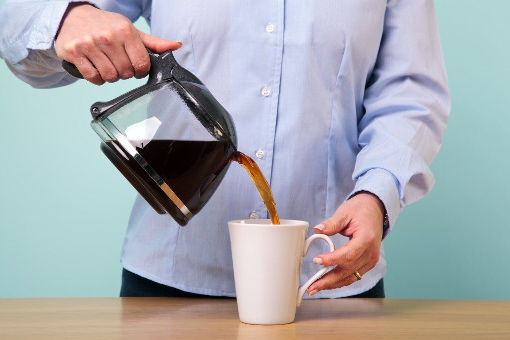 Photo of a woman on her break pouring herself a mug of hot filtered coffee from a glass pot.