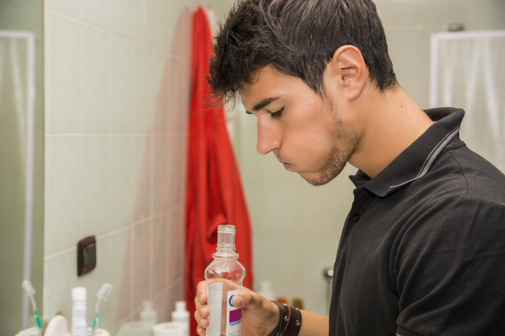 Young man wearing black t shirt using mouthwash in bathroom 