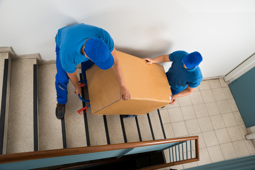 Two Male Movers Walking Downward With Box On Staircase