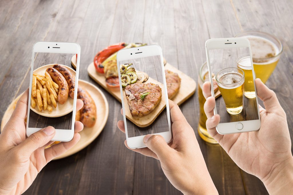 Three hand holding phones while taking pictures of food and drinks
