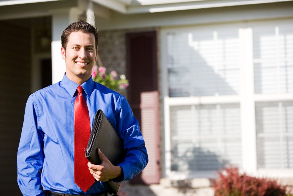 Man Holding portfolio file in front of house smiling