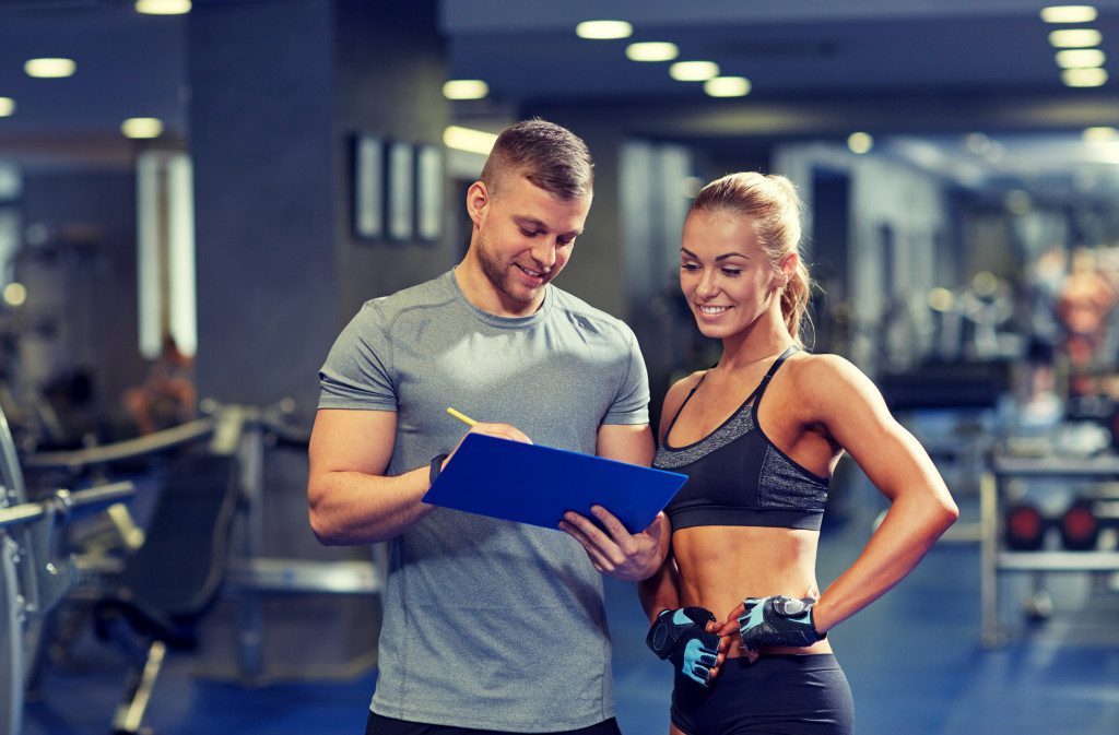 A male gym instructor is showing some credibility documents to her female gym client.
