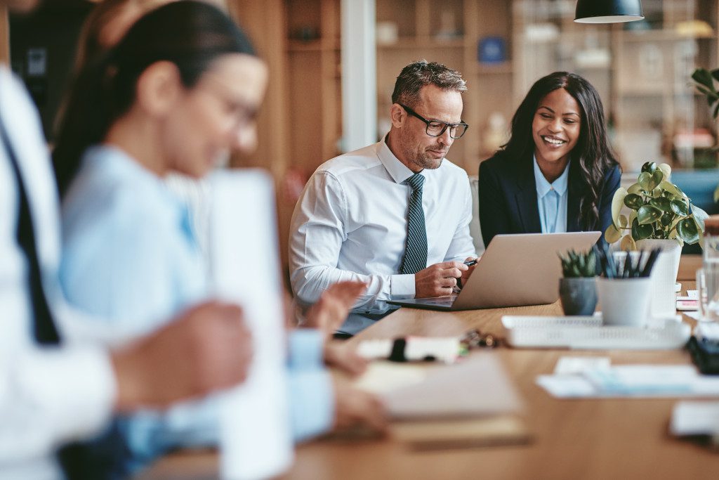 Two diverse businesspeople smiling while working on a laptop together at the end of a boardroom table in an office