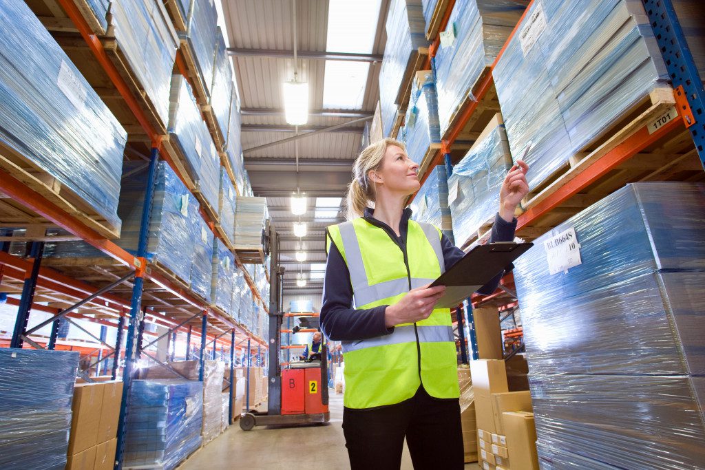 A low angle medium shot of a female warehouse worker holding a clipboard and checking inventory.