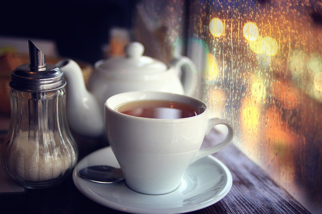 A cup of tea, a teapot, and sugar near a wet window