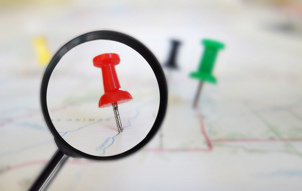 A magnifying glass surveying push pins tacked on a map