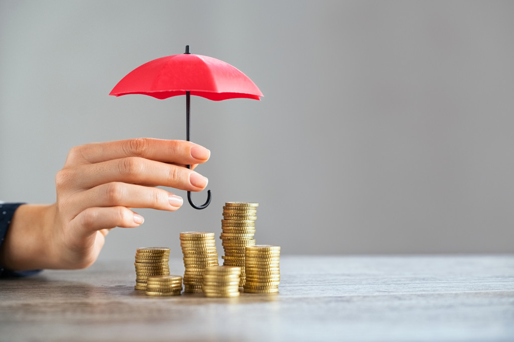 Young woman hand holding small red umbrella over pile of coins on table