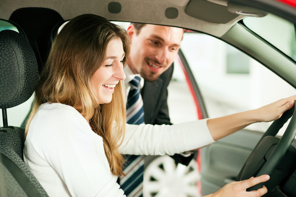 car dealer smiling with female driver smiling inside financed car